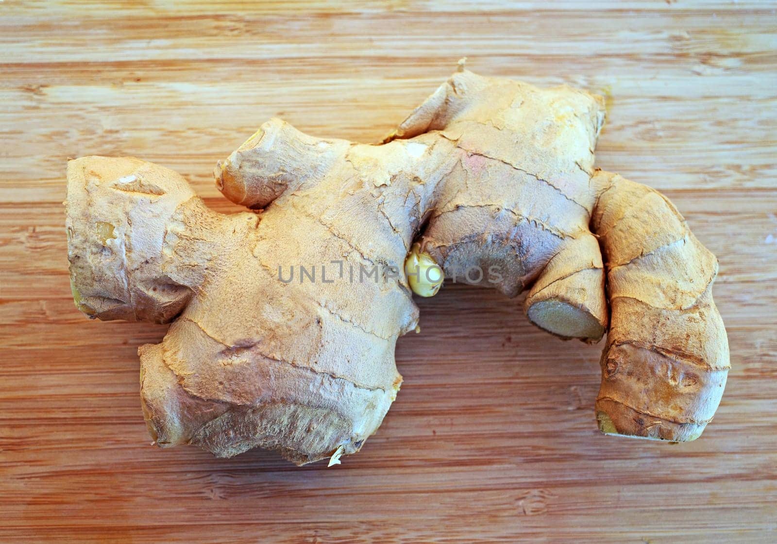 Part of an irregularly shaped fresh ginger root on a wooden cutting board. Top view