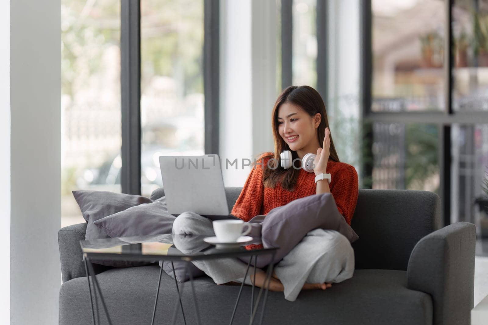 Beautiful Asian Woman smile and relaxing at home and using laptop computer sitting on cozy sofa by itchaznong