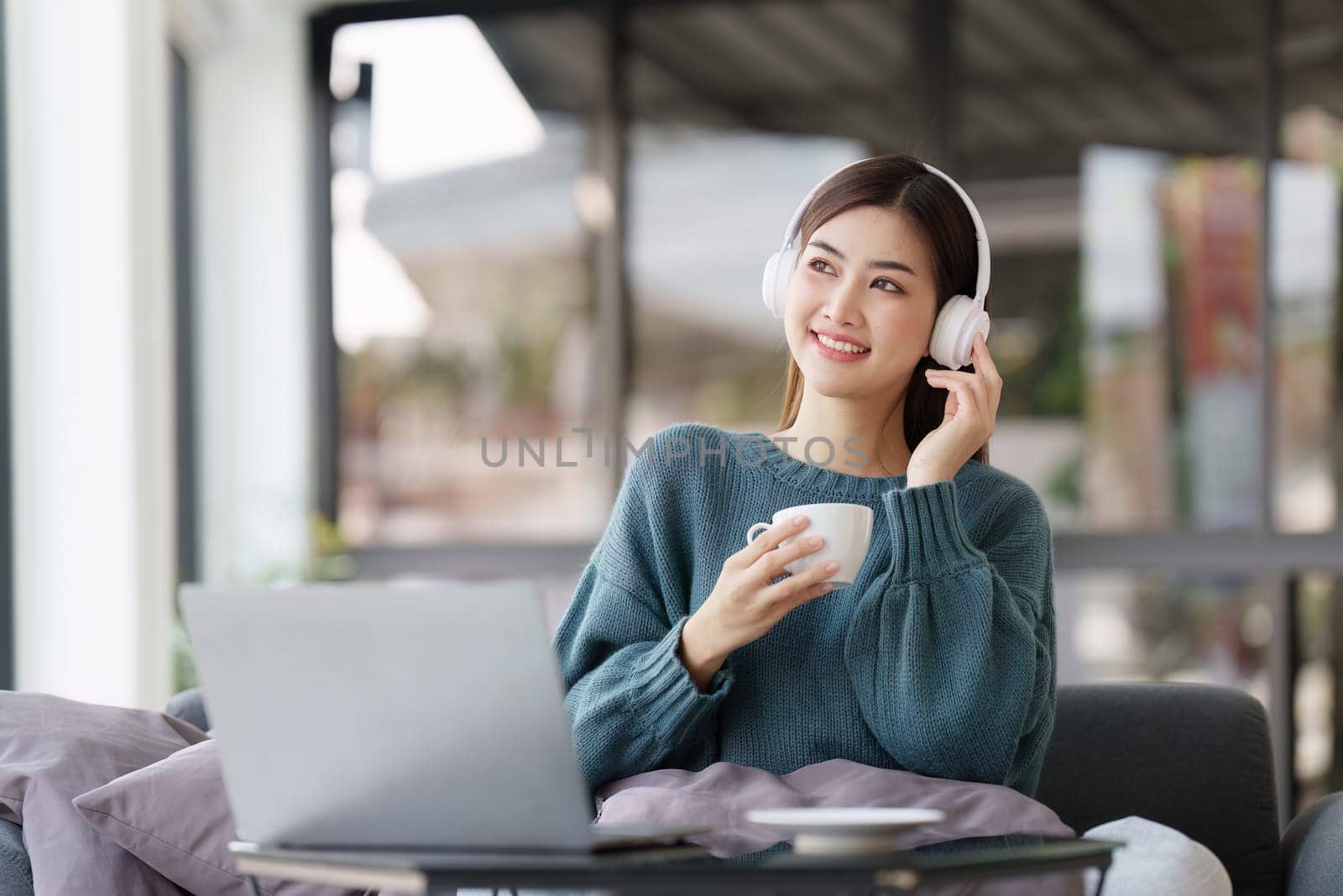 Beautiful Asian Woman smile and relaxing at home and using laptop computer sitting on cozy sofa.