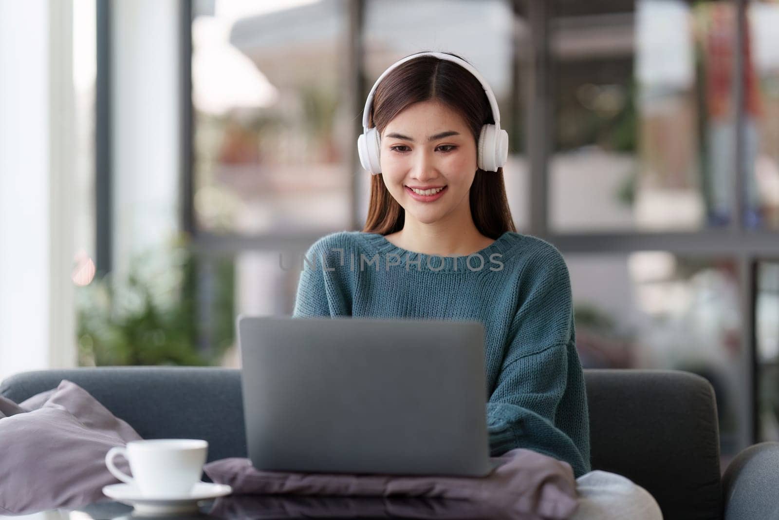 Beautiful Asian Woman smile and relaxing at home and using laptop computer sitting on cozy sofa by itchaznong