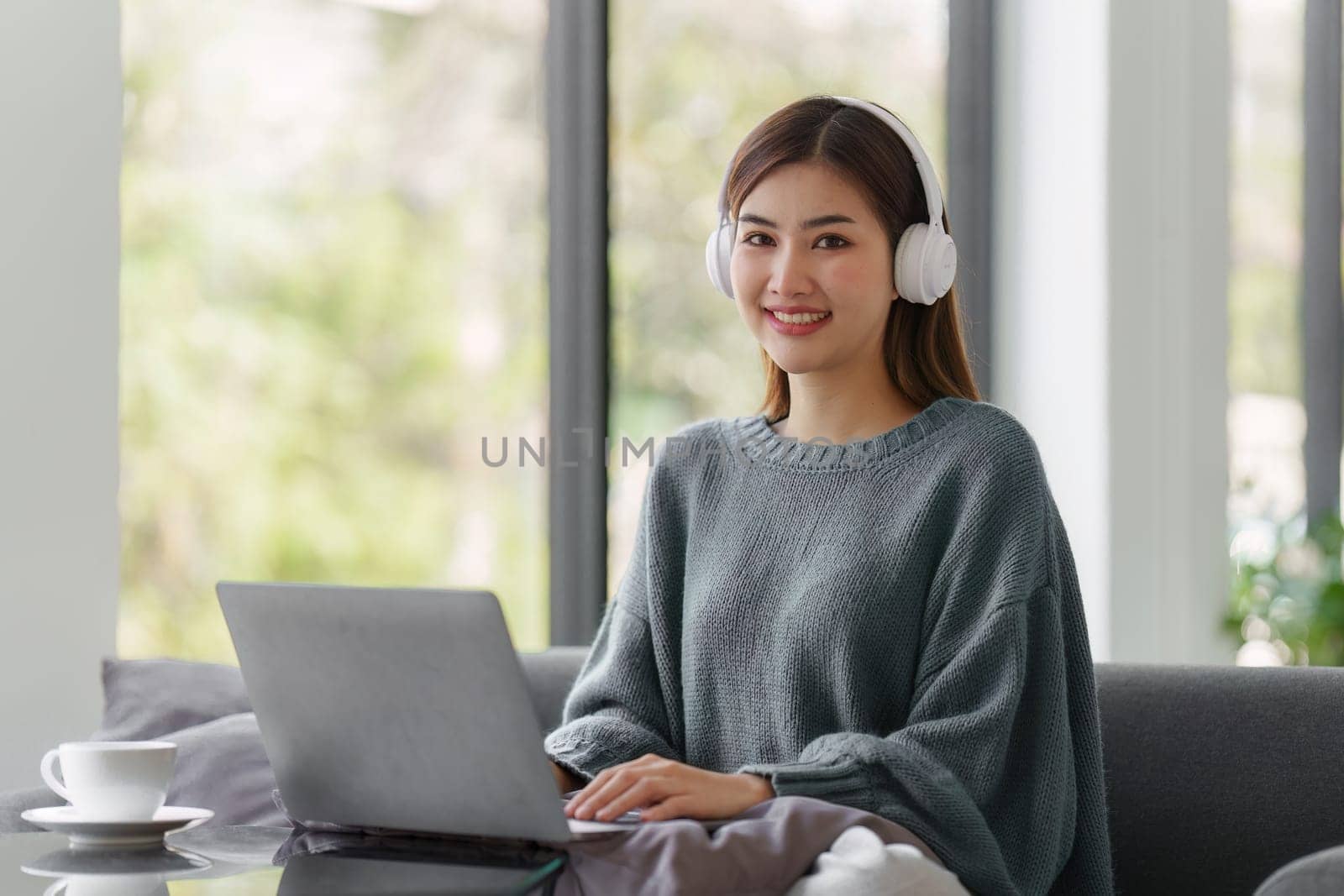 Beautiful Asian Woman smile and relaxing at home and using laptop computer sitting on cozy sofa by itchaznong