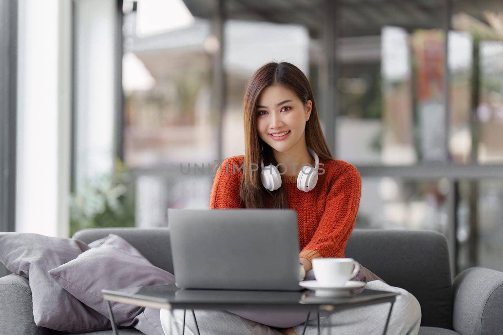 Beautiful Asian Woman smile and relaxing at home and using laptop computer sitting on cozy sofa by itchaznong