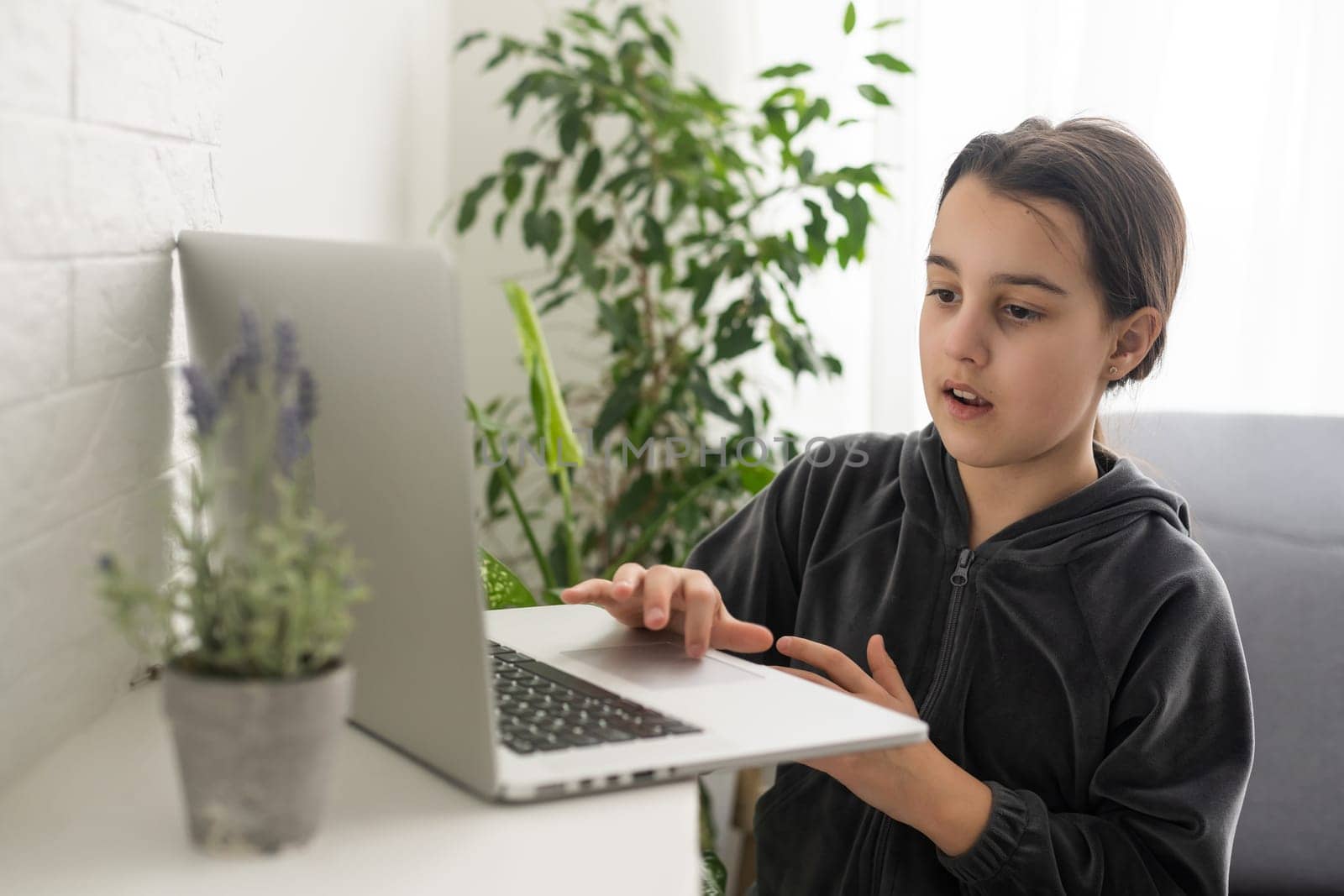 A teenage girl sits in front of her laptop learning sign language, a language for the deaf online.