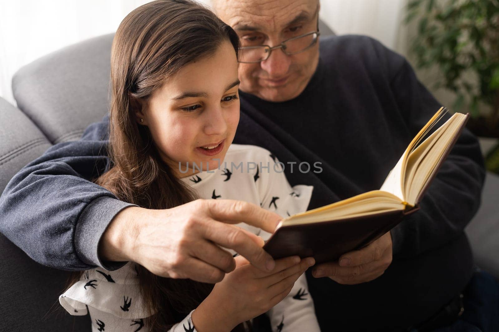 Book, family and children with a girl reading to her grandfather on the floor of their living at home. Kids, read and story with a senior man and granddaughter bonding in their house during a visit. by Andelov13