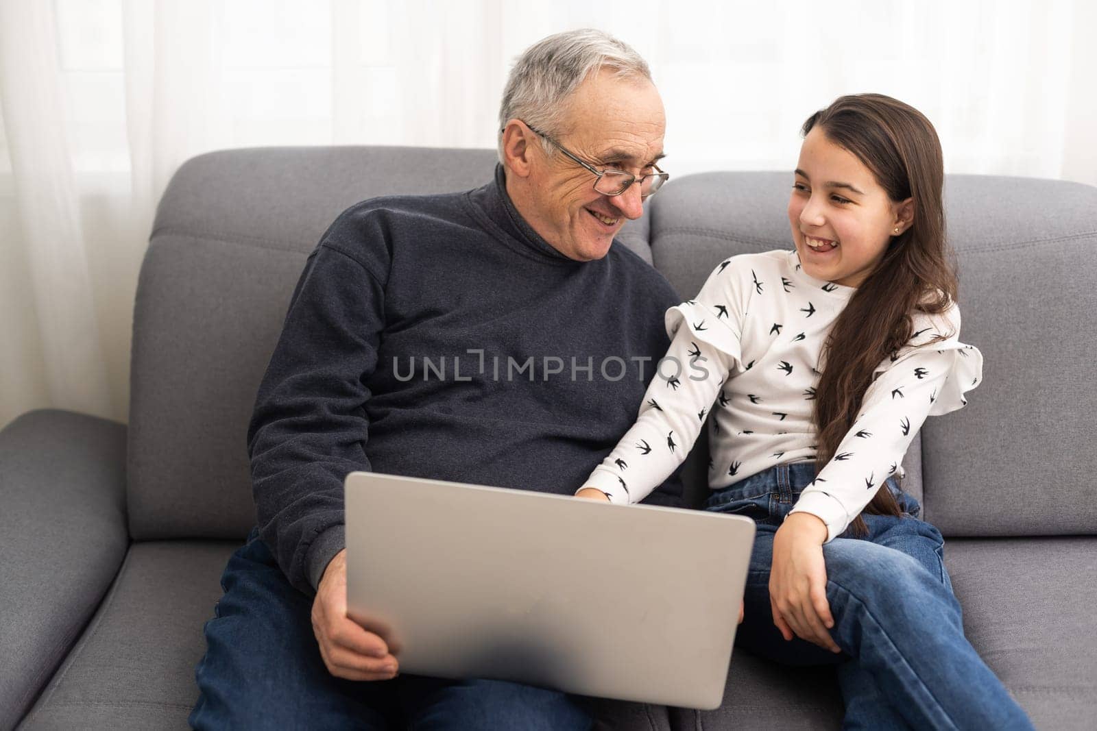 Happy retirement grandfather and pretty granddaughter laughing while watching e-book for learning to education together by laptop. Family educational at home concept. Technology and education