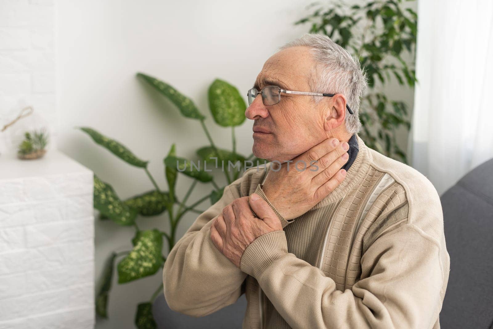 Old man with toothache. Elderly senior man has toothache. Unhappy man face in tooth pain sitting on sofa at home, feel sick unwell. Sad aged man hand holding his chin. Adult suffering toothache by Andelov13