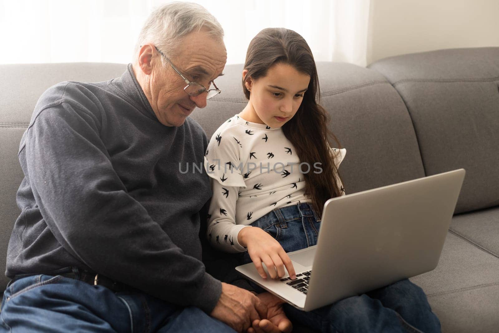 Adorable little girl and happy grandfather using laptop at home by Andelov13