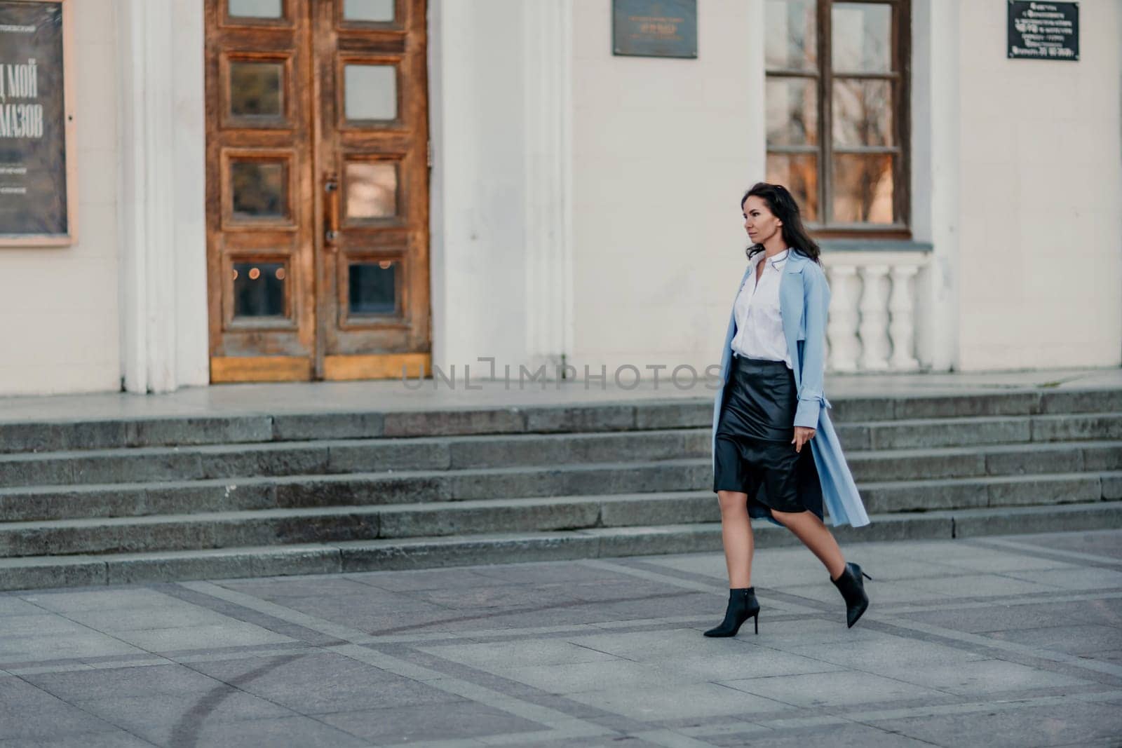Woman walks in the city, lifestyle. Young beautiful woman in a loose light sweater, brown skirt and sneakers with a hat