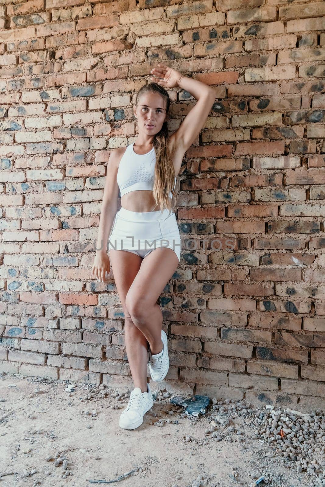 A mid-30s happy woman with long hair natural color poses in her underwear, smiling in front of a brick wall on a construction site for model tests by panophotograph