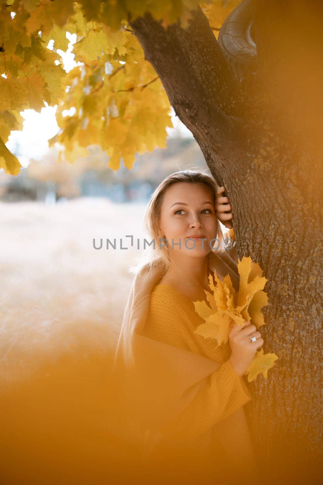 The blonde stands near the autumn tree. Thoughtful woman looks ahead, dressed in a yellow dress. Autumn content by Matiunina