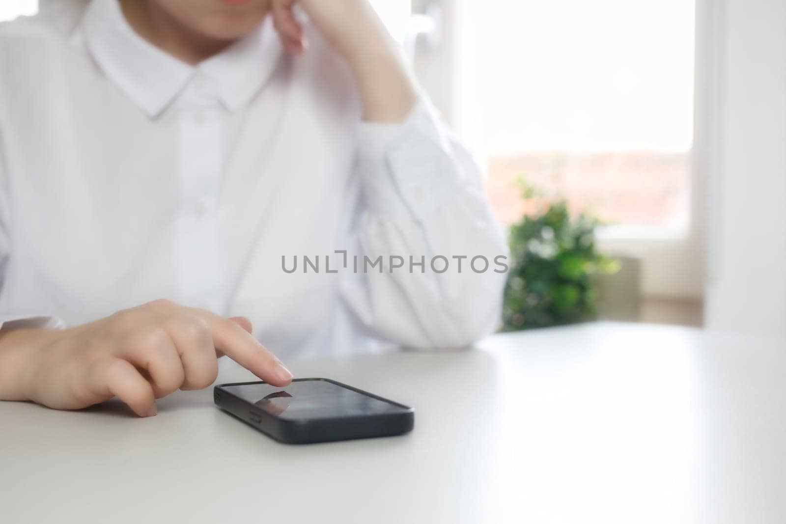 Hands of young woman using online app on mobile phone, making call, browsing Internet, chatting on social media, holding cellphone, texting, typing message. Close up on white desk bright colors scrolling