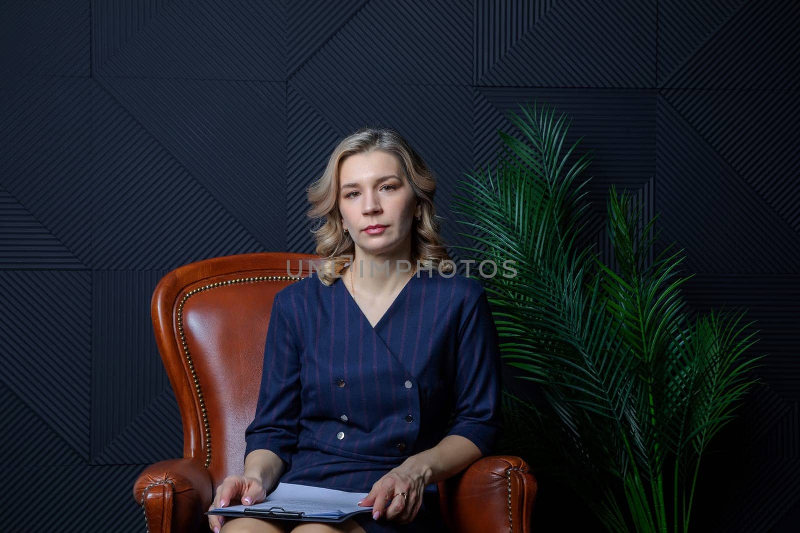 Portrait of a successful female psychologist in her office, notebook in hand, in her chair