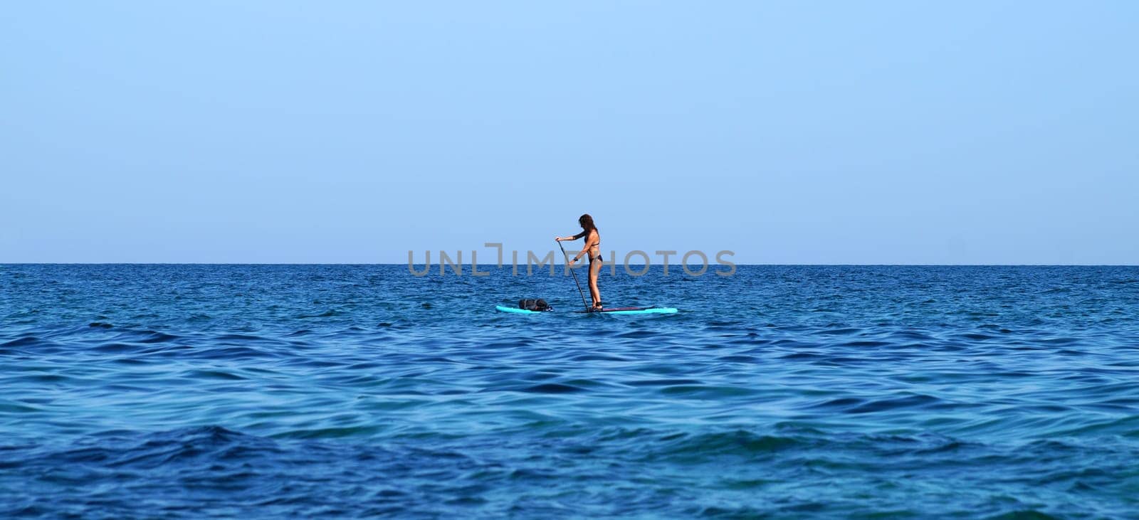 A woman standing on a SUP board with an oar floats on the sea by Annado