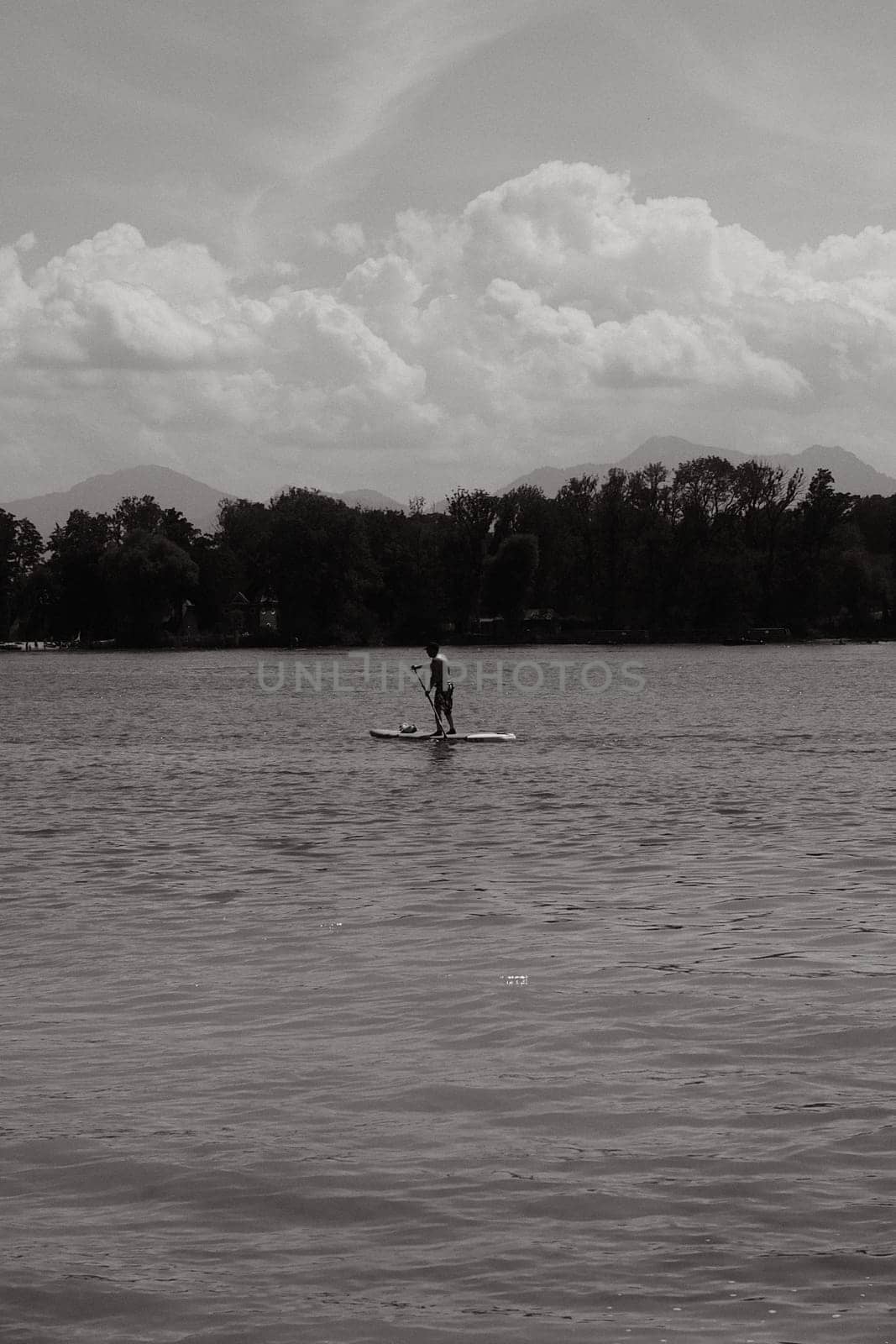 Grayscale shot of a man paddleboarding on Chiemsee lake in Bavaria, Germany on a sunny day