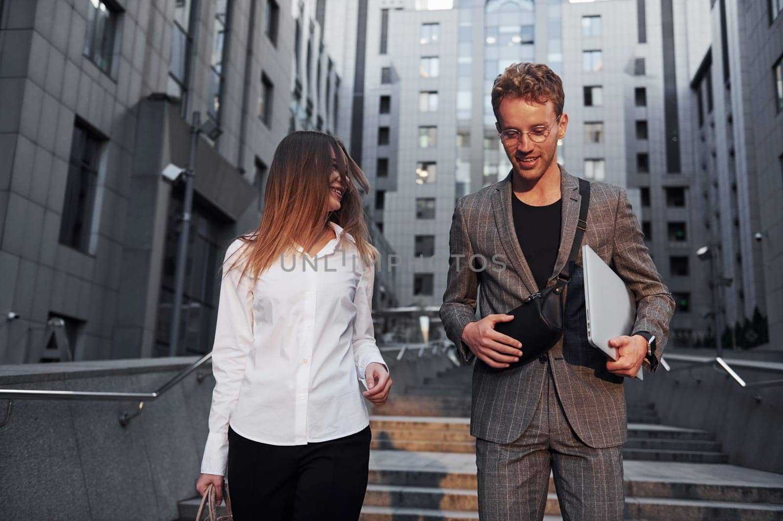 Closed laptop in hands. Woman and man in the town at daytime. Well dressed people by Standret