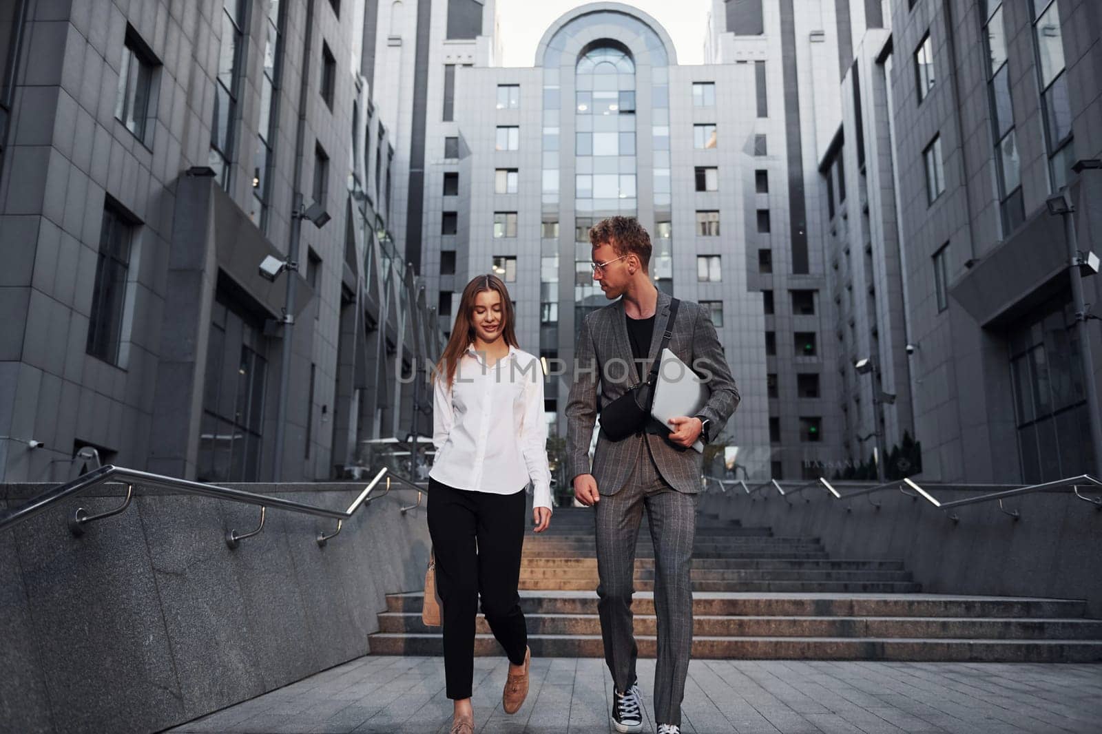 Closed laptop in hands. Woman and man in the town at daytime. Well dressed people by Standret