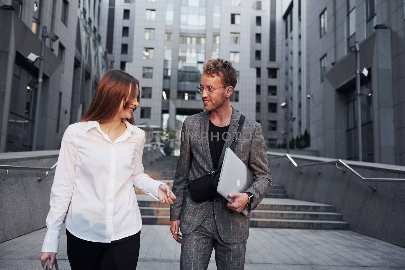 Closed laptop in hands. Woman and man in the town at daytime. Well dressed people by Standret