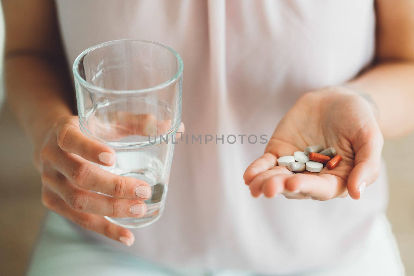 Close up woman holding vitamin pills in one hand and a glass of water in other by VisualProductions