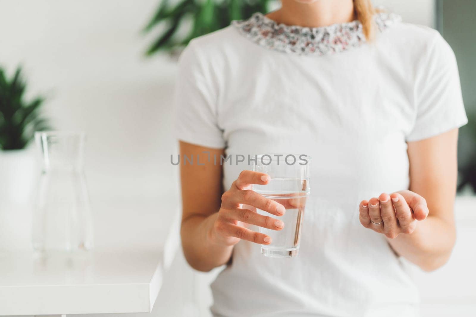 Unrecognizable woman close up holding a glass of water in one hands and vitamin pills in the palm of her other hand by VisualProductions