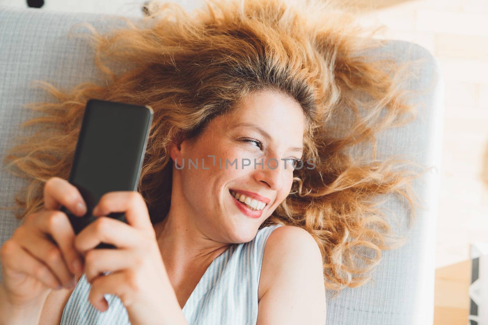 Close up portrait of a woman with curly hair looking away laying down on the couch while holding her phone up in the air taking selfies by VisualProductions