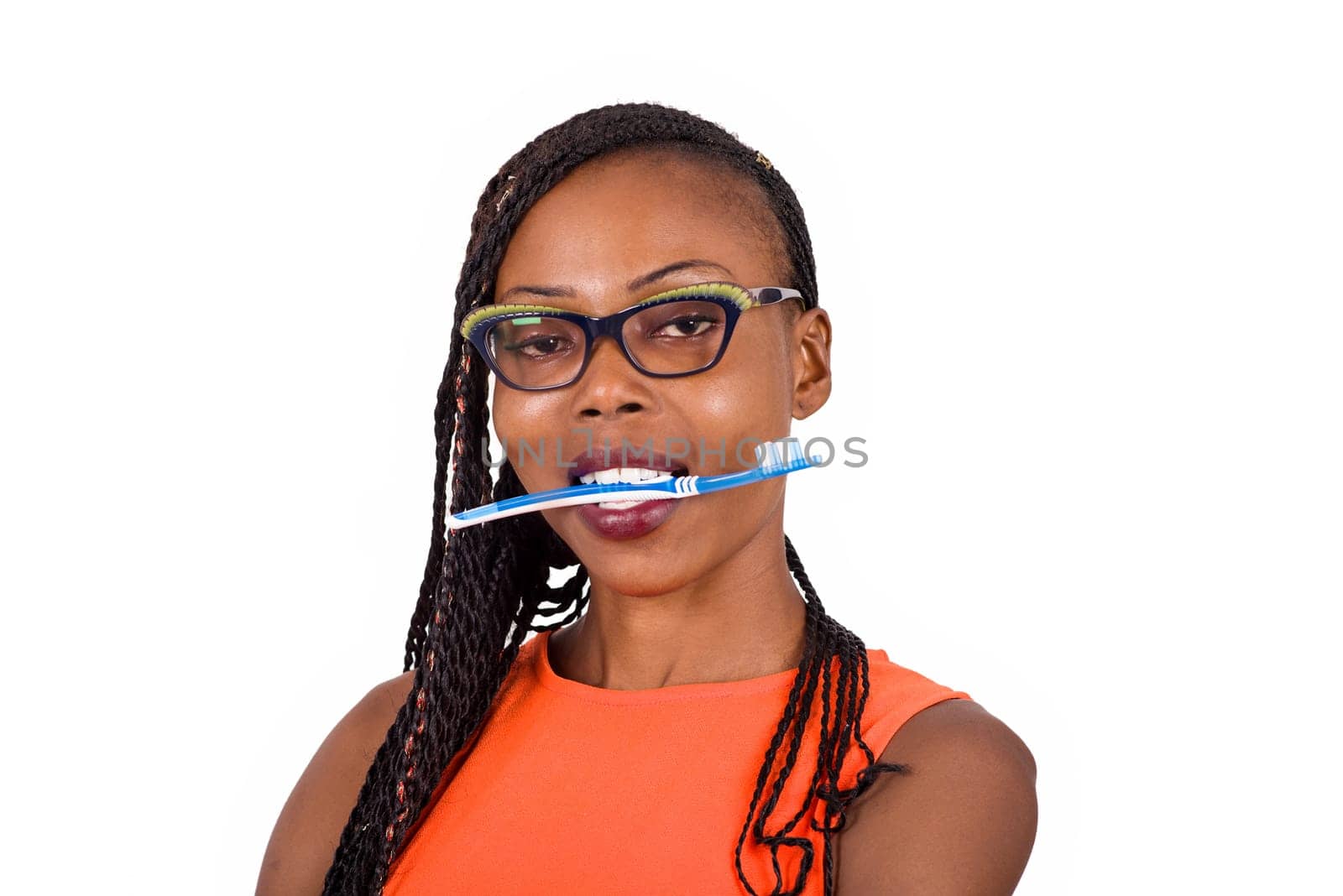 young girl standing in glasses watching the camera while biting a toothbrush.