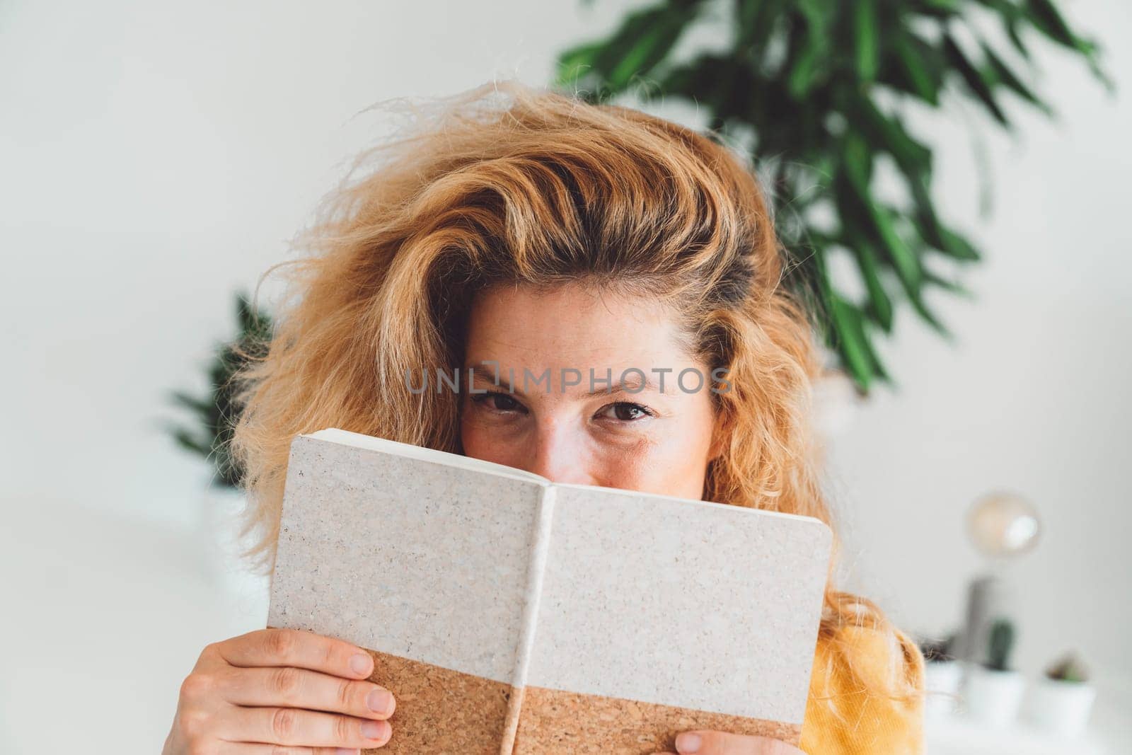Playful blonde woman hiding half of her face behind a note book by VisualProductions
