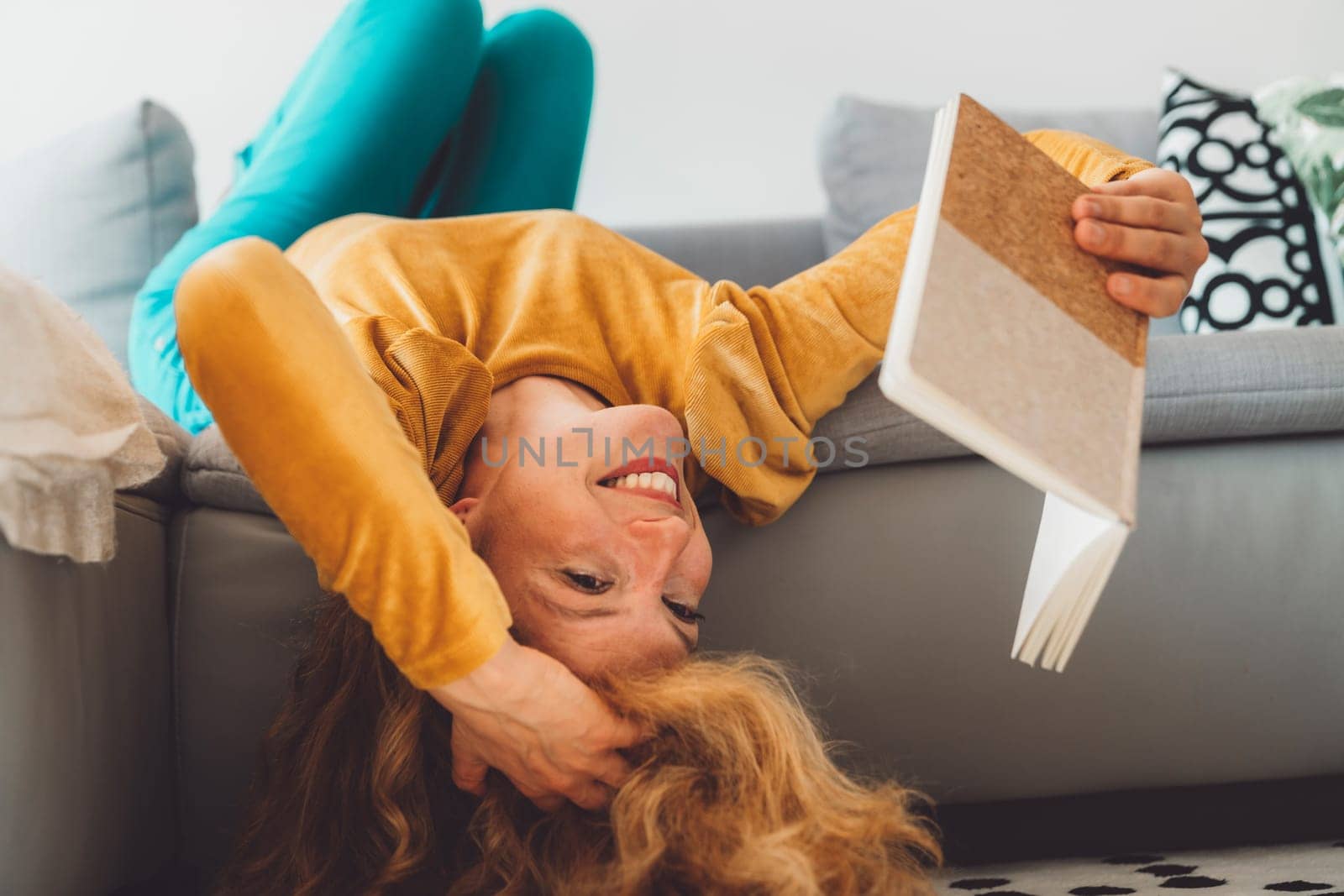 Trying to read upside down - Playful blonde curly woman reading a book on the couch by VisualProductions