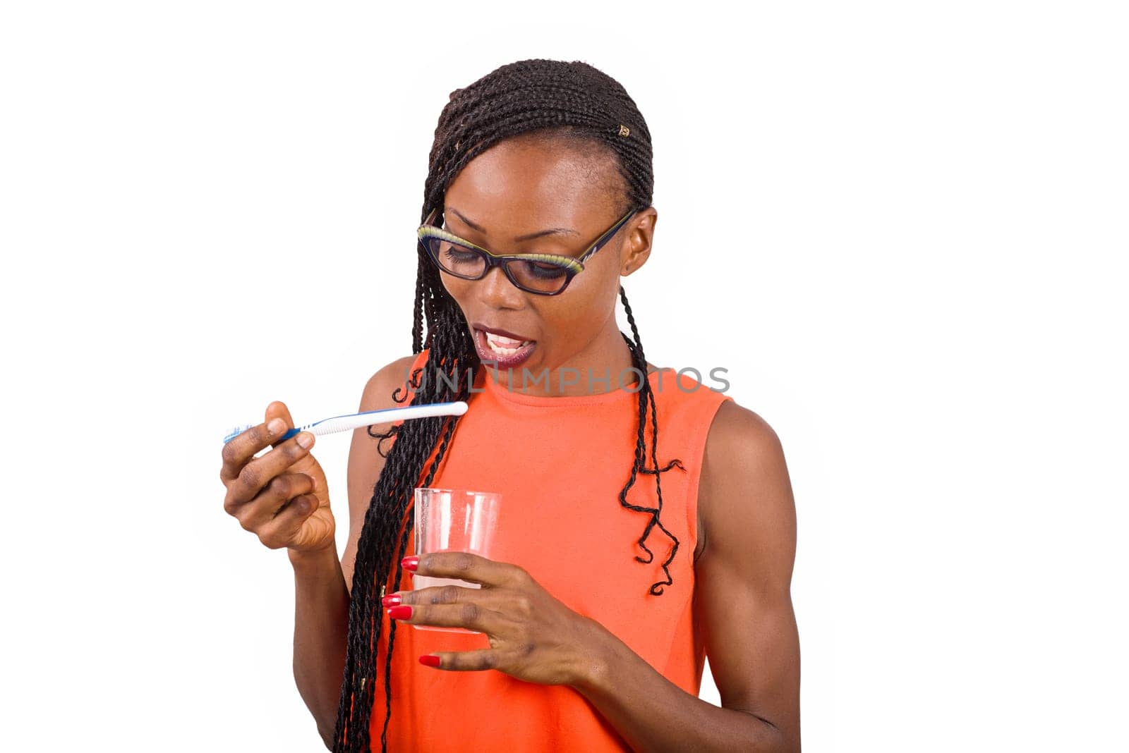 young girl standing in glasses looking at a glass with toothbrush in hand.