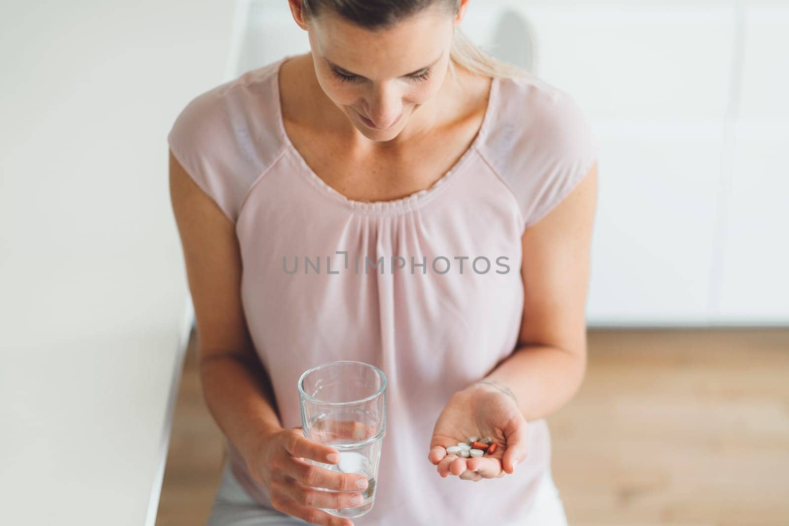 Caucasian woman holding a bunch of pills in one hand and a glass of water in other, top down view by VisualProductions
