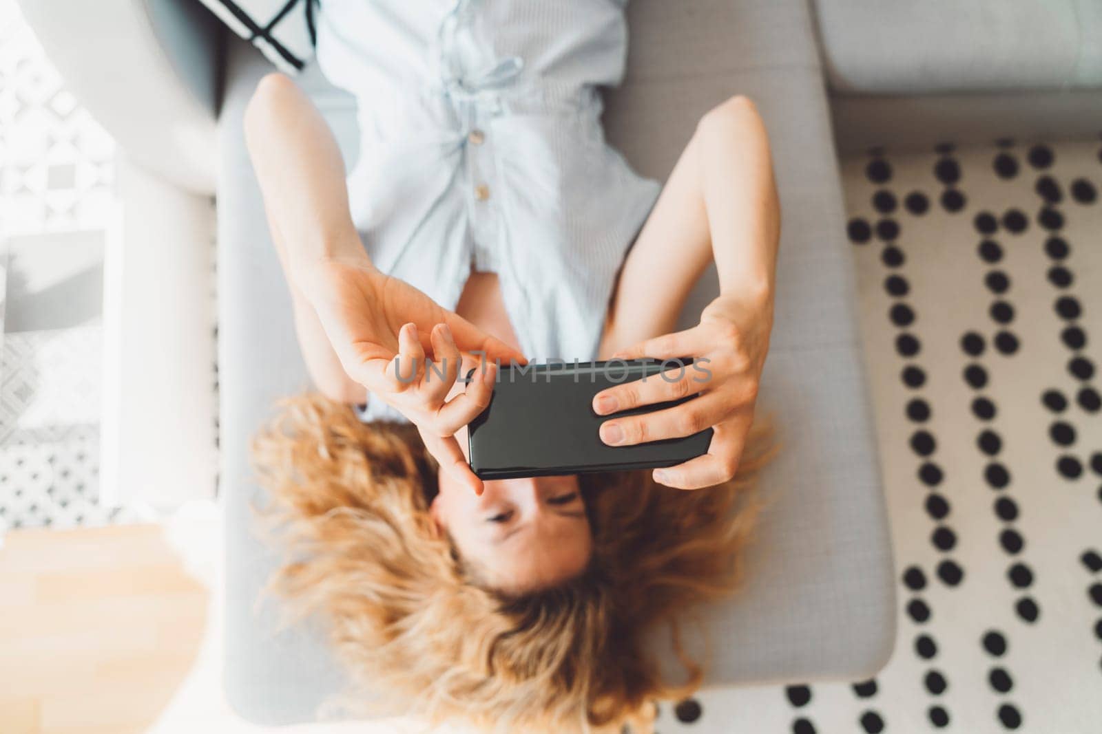 Top down view, blurred woman laying on the grey sofa taking selfies with her phone by VisualProductions