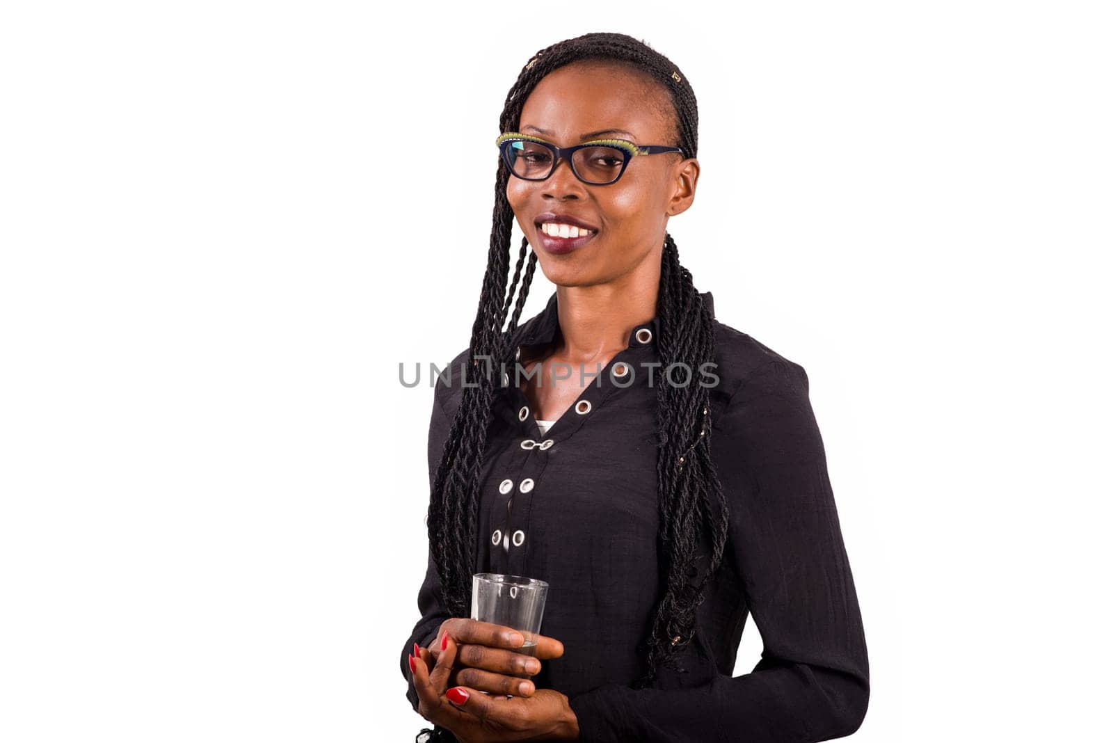 young woman standing on white background in eyeglasses to look at the camera smiling with glass of water in hand.
