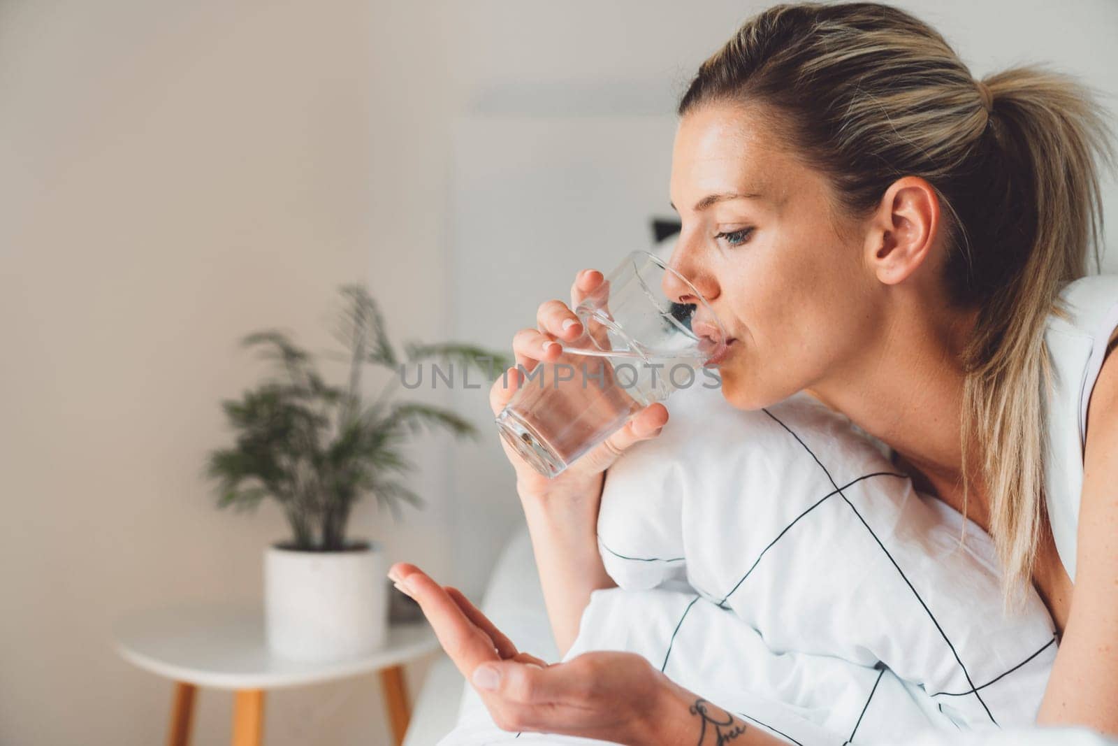 Side portrait of blonde woman taking her morning vitamins while still in bed by VisualProductions