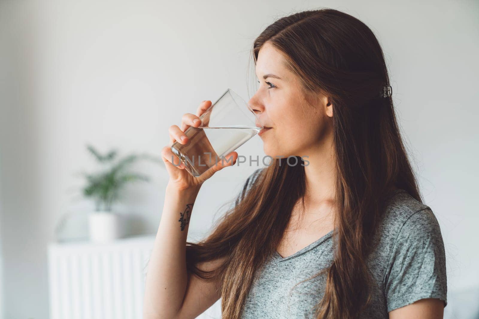 Waist up side portrait young brunette drinking a glass of water on white background by VisualProductions