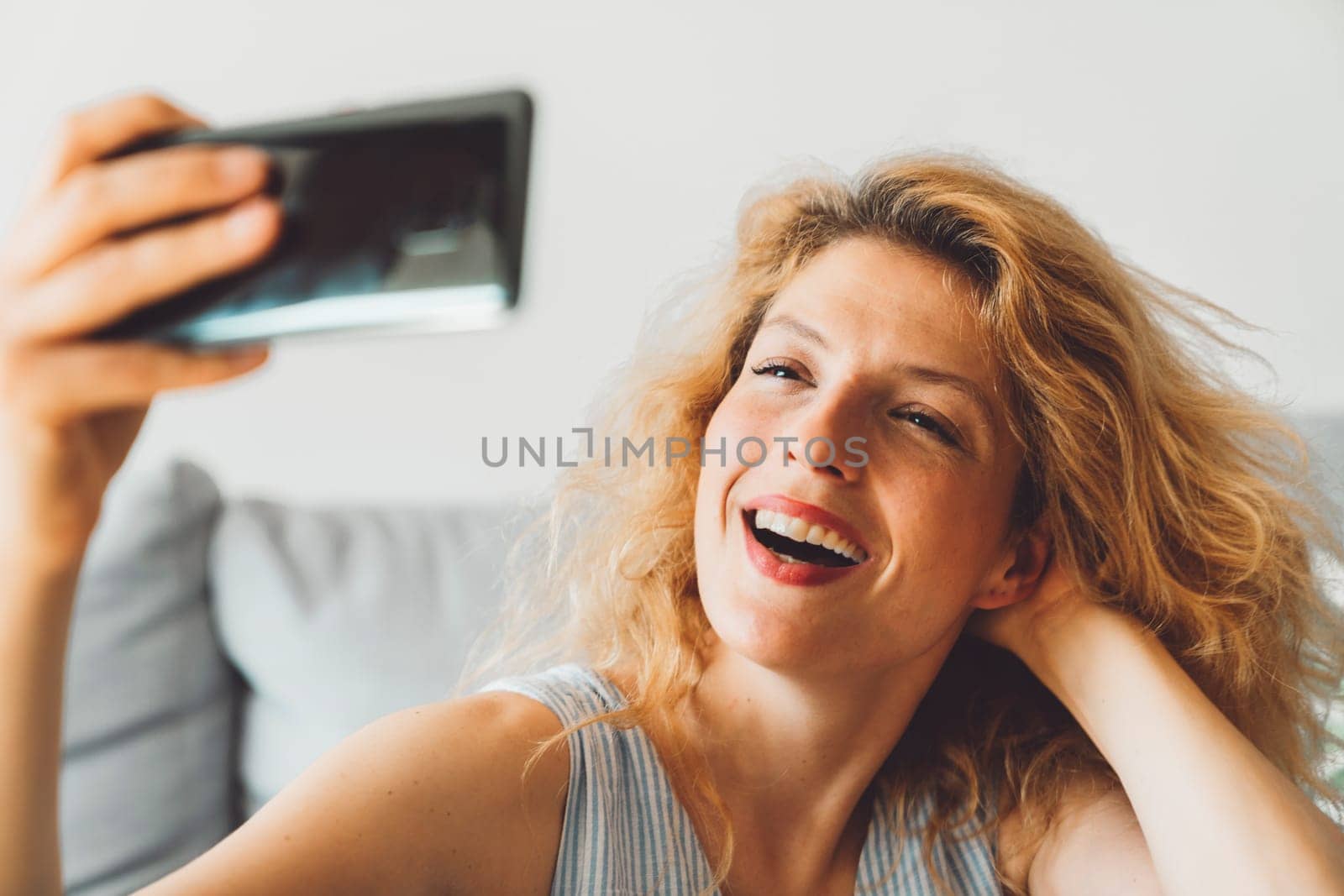 Close of portrait of smiling curly woman taking selfies with her phone by VisualProductions