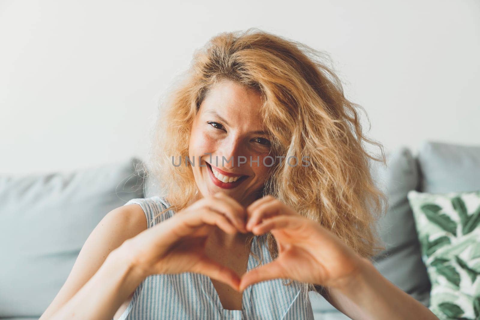 Waist up portrait of a smiling woman with curly hair holding hands in a heart shape by VisualProductions