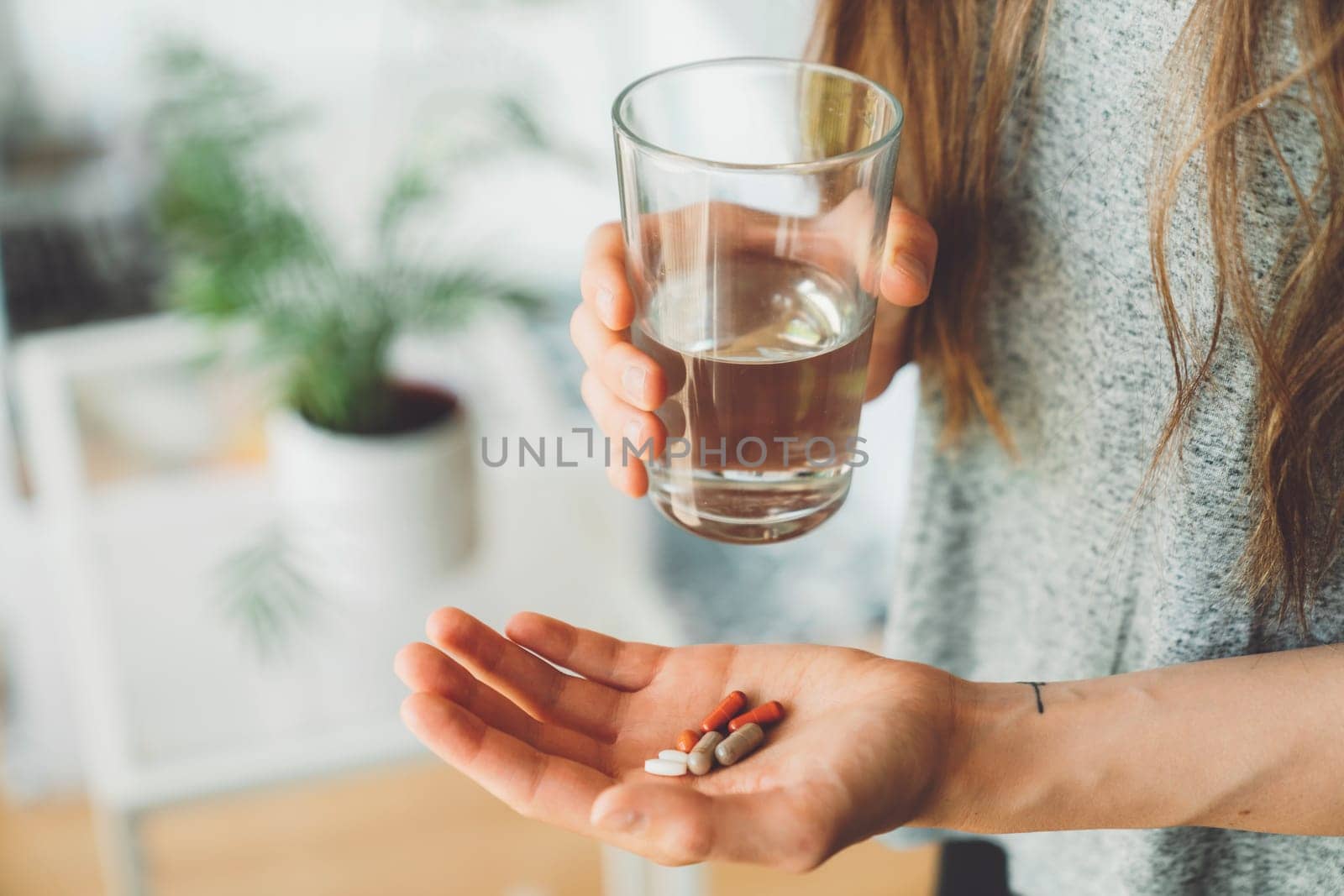 Unrecognizable woman holding supplement pills in one hand and a glass of water in other by VisualProductions