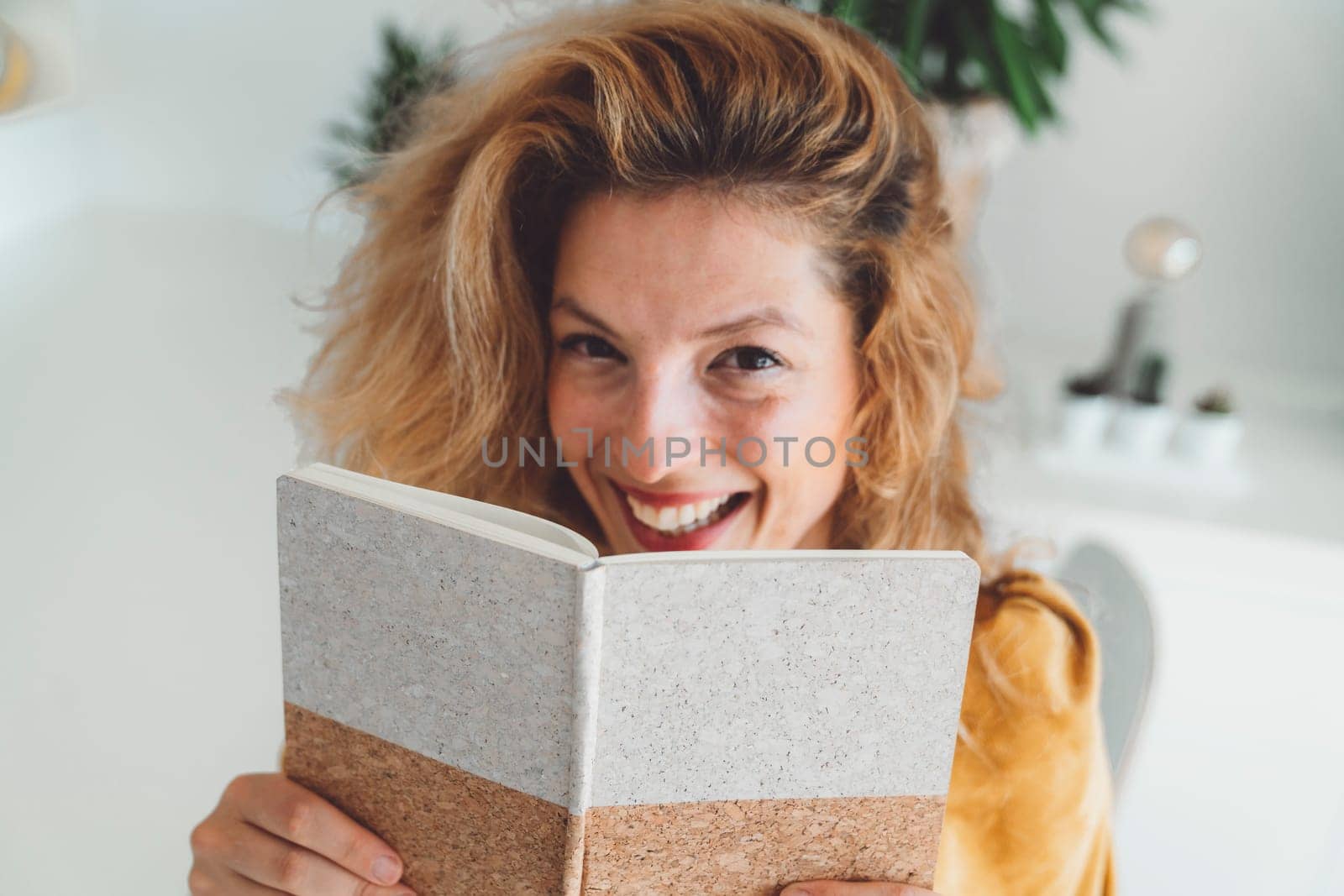 Waist up portrait of a smiling woman hiding behind her notebook by VisualProductions