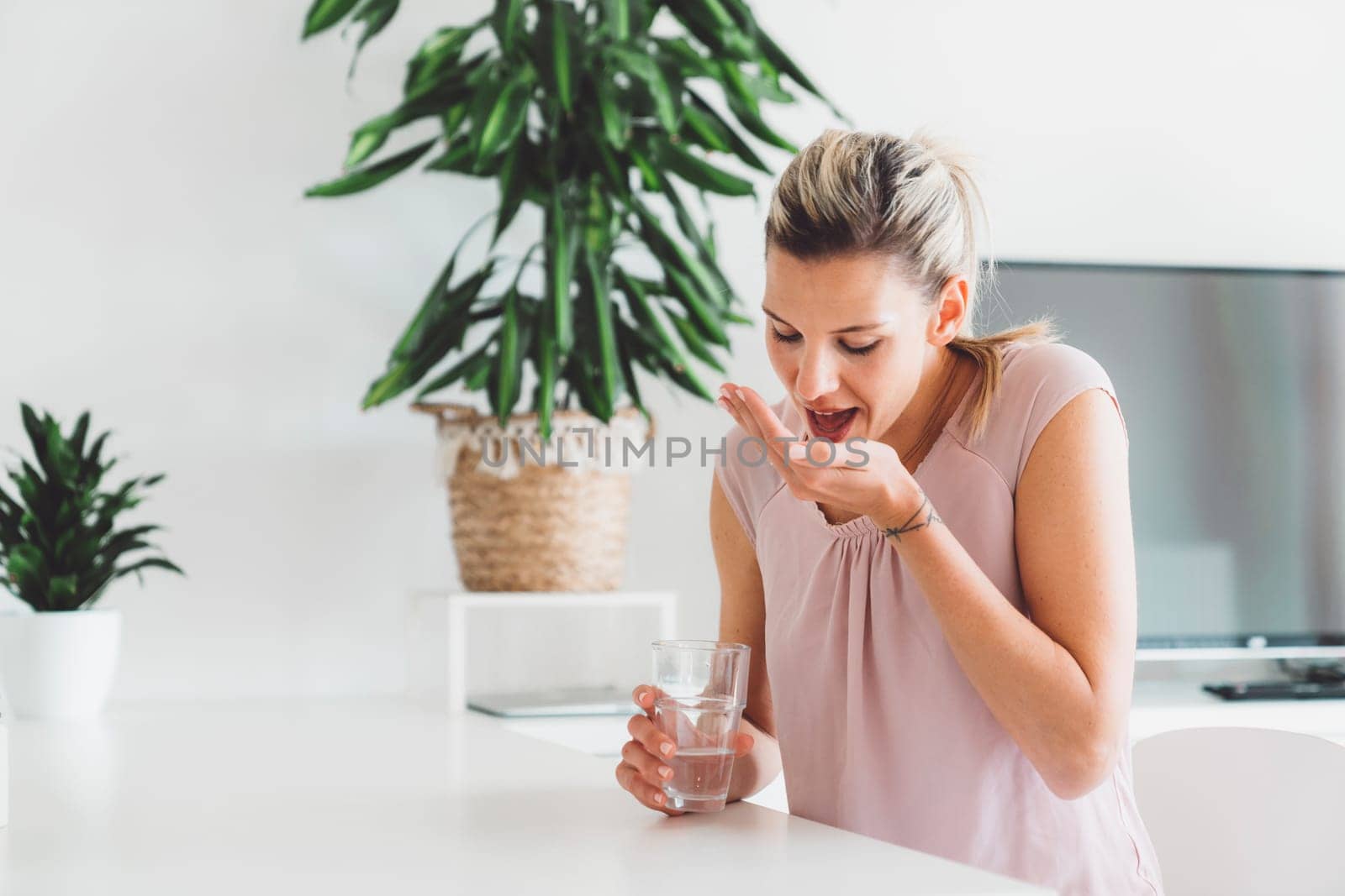 Woman taking her vitamin pills while sitting by the dining room table at home by VisualProductions