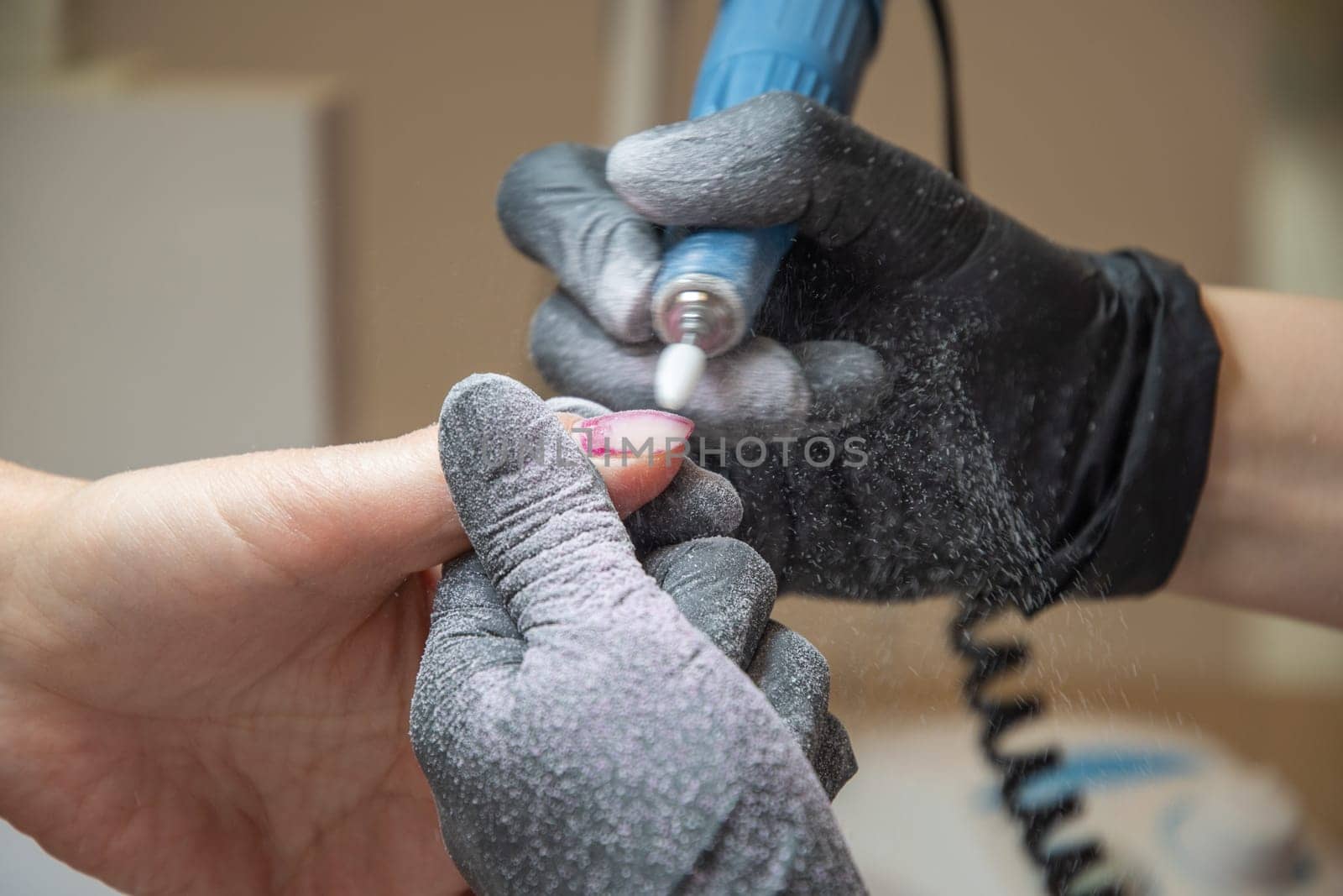 The manicurist grinds off the old coating from the client's nails with the help of a professional electric nail file. High quality photo