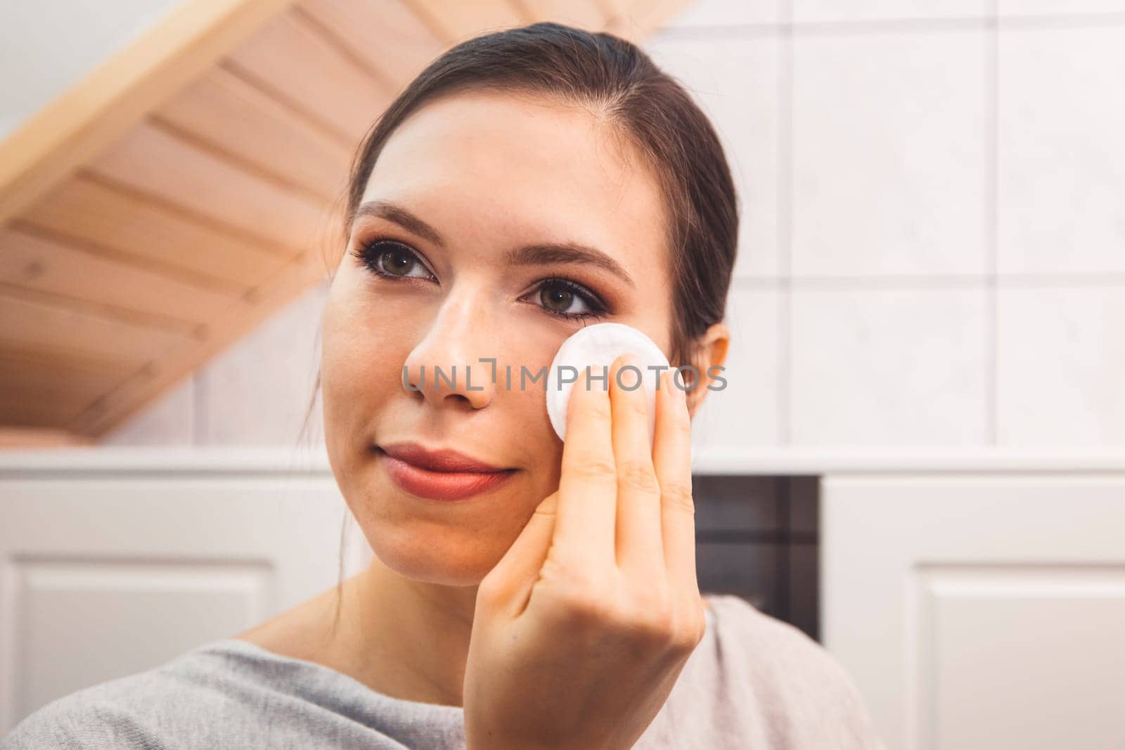 Waist up close up portrait of a young woman removing make up in her bathroom at night by VisualProductions