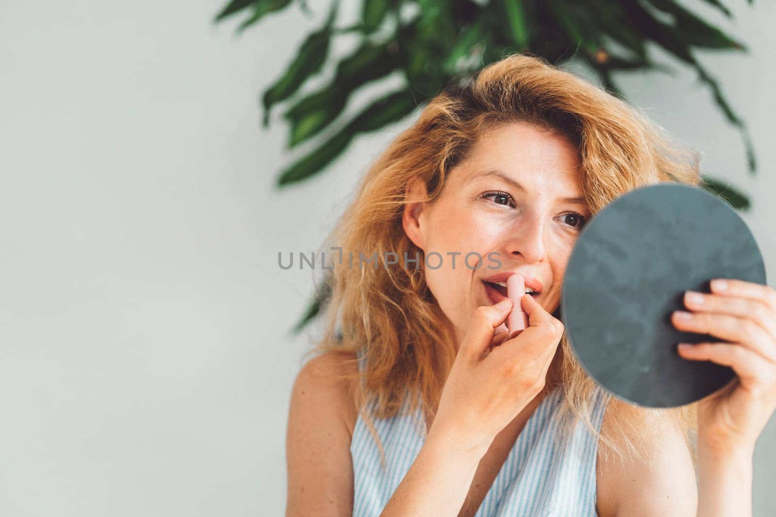 Wait up portrait of a woman doing her lipstick, looking at the small round mirror she is holding up by VisualProductions