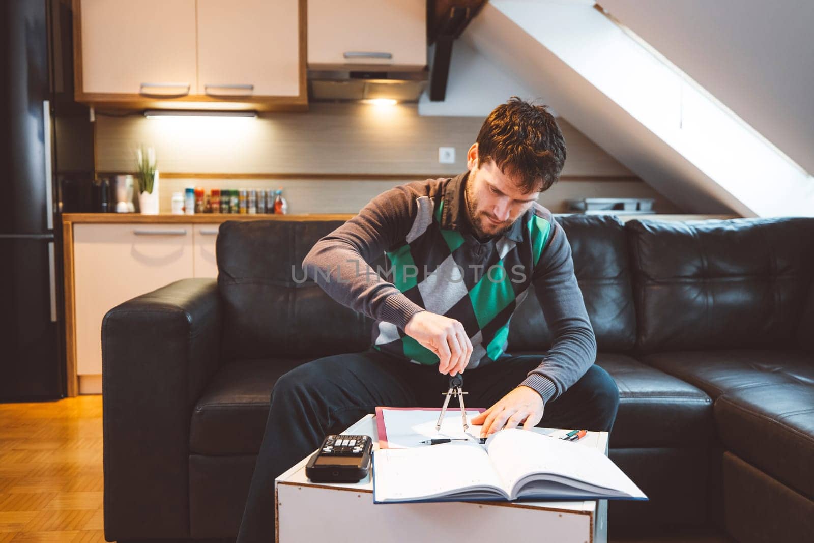 Bearded man physics student sitting on the sofa studying at home by VisualProductions