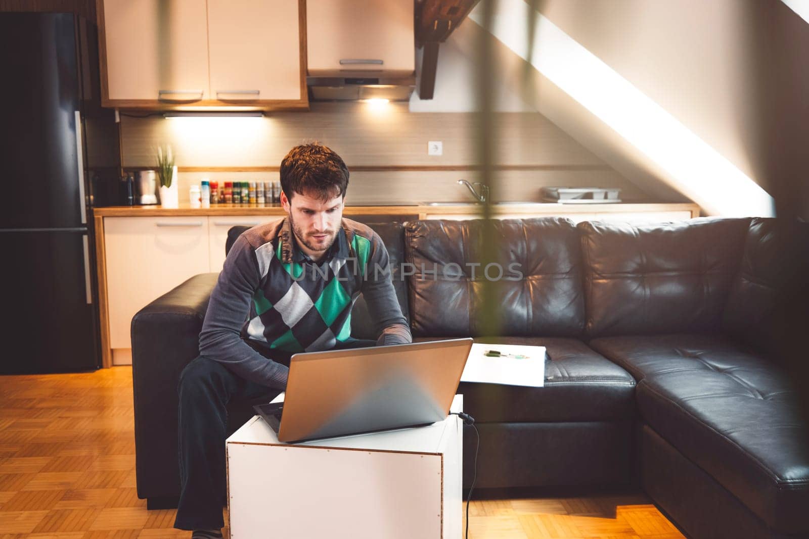 Bearded caucasian man studying on his laptop, online working from his apartment while sitting on the sofa by VisualProductions