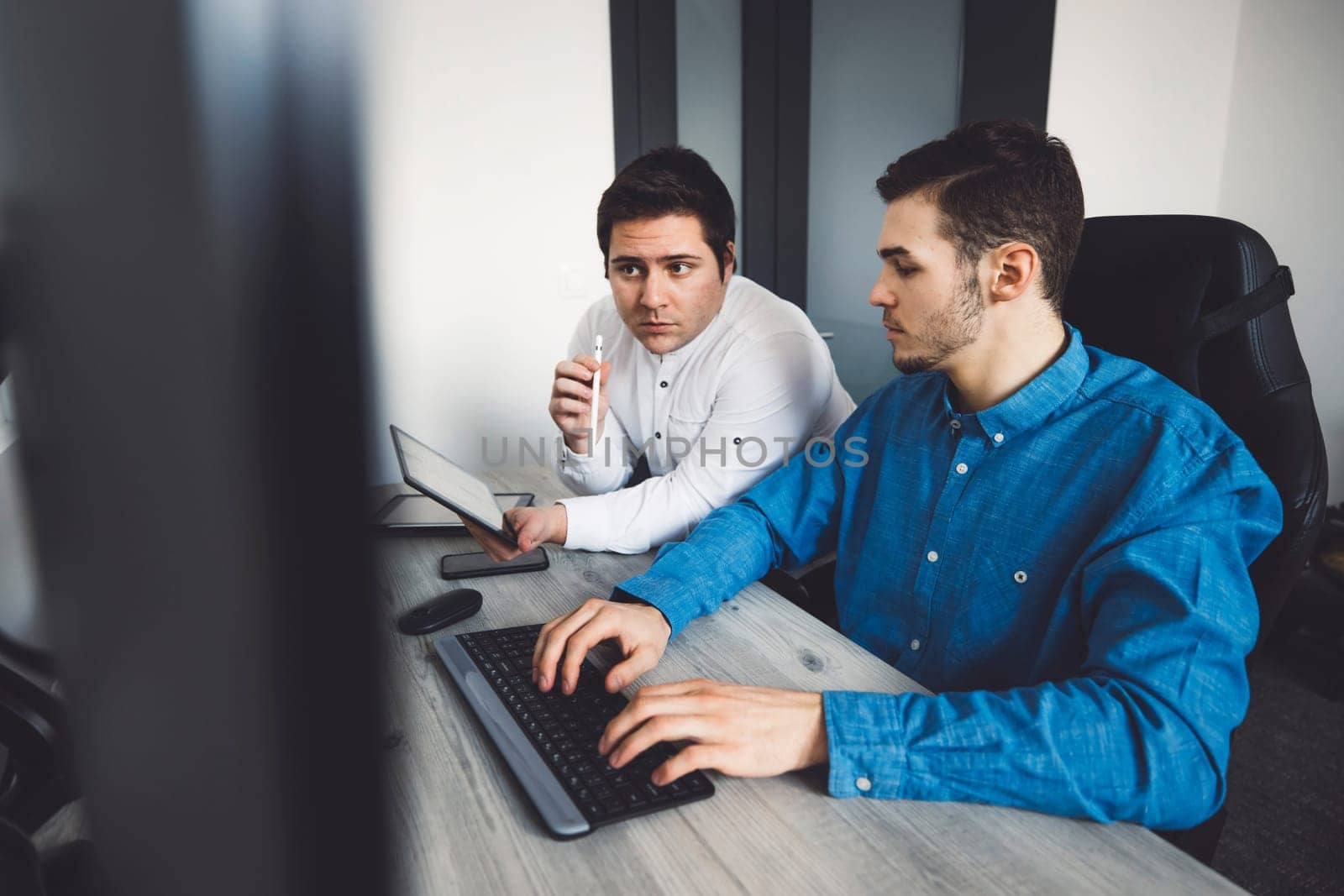 Two young caucasian programmers working on desktop computers in the office developing a new video game by VisualProductions
