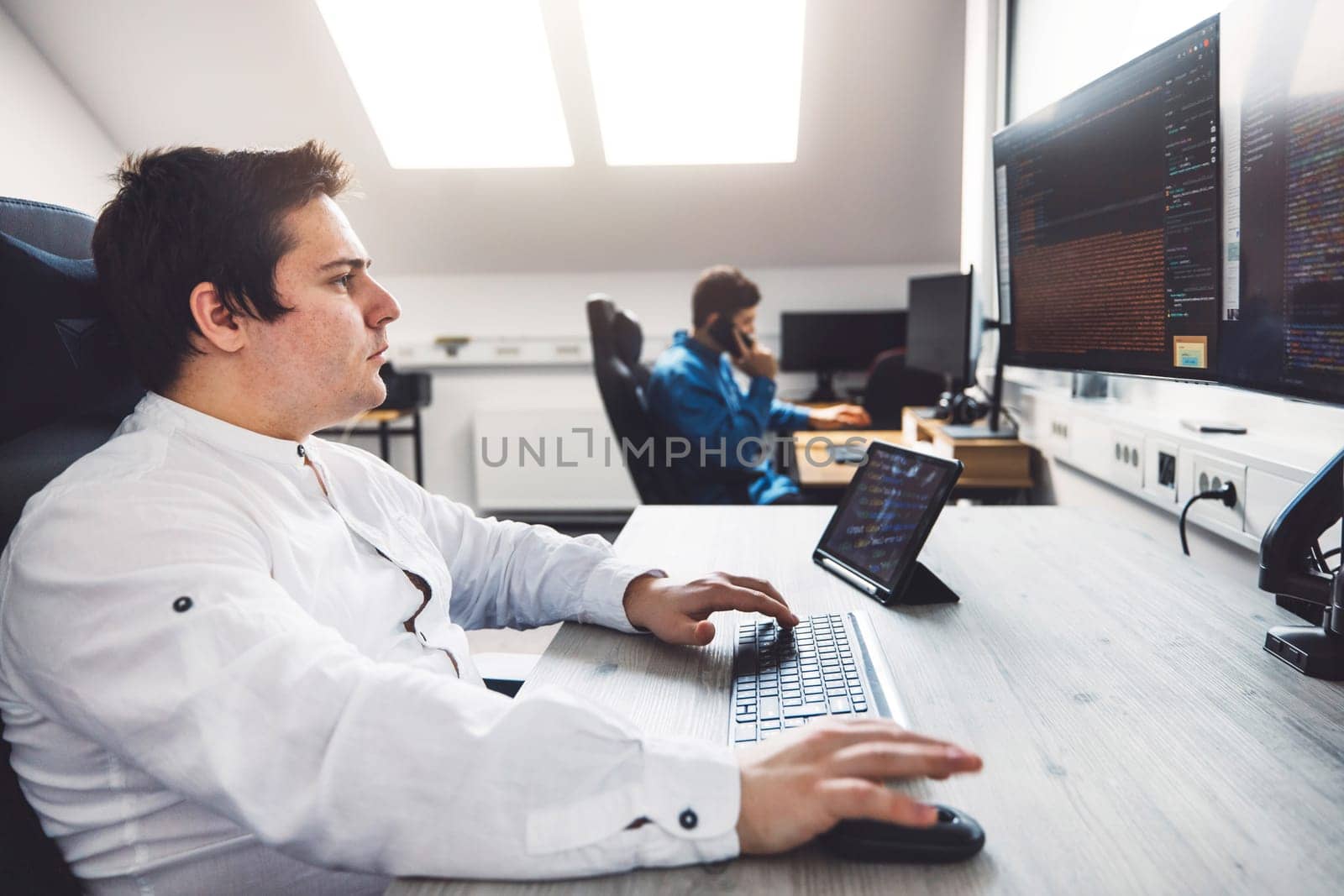 Side view waist up of two IT programmers coding in a bright office with lost of natural light by VisualProductions