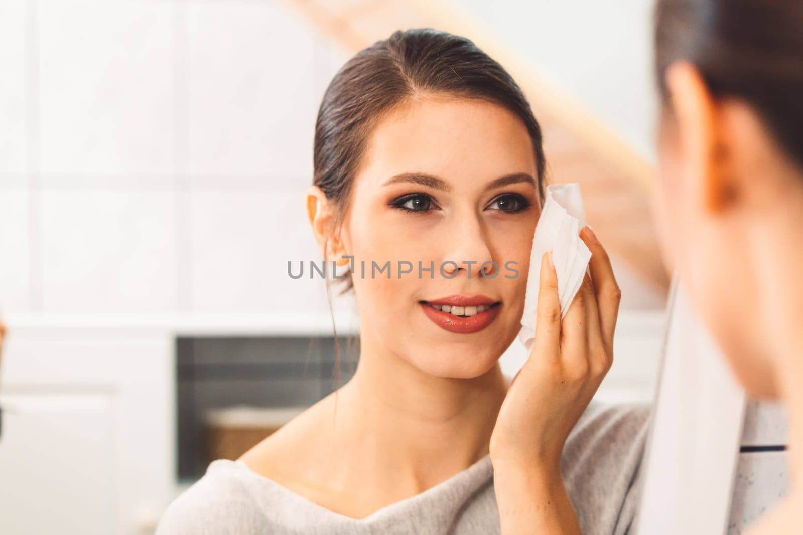 Close up over the shoulder view of young woman cleaning her face with a cotton pad in the evening in her bathroom by VisualProductions