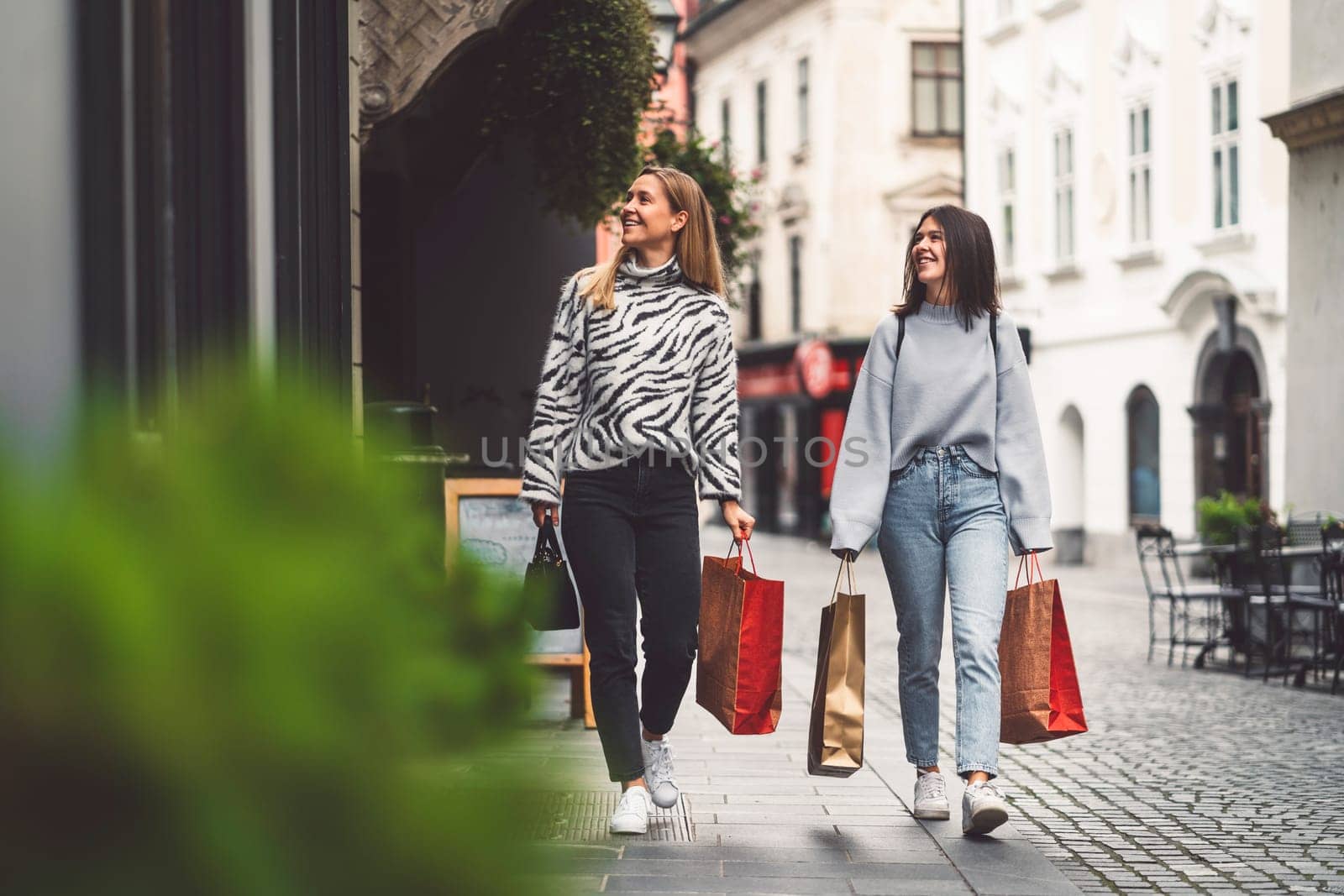 Two young women on a shopping spree in the city center, walking around with paper shopping bags in their hands by VisualProductions