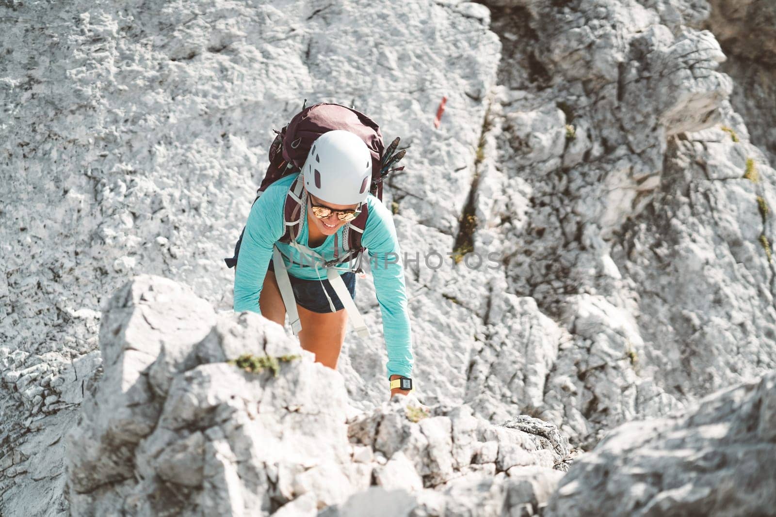 Looking down at woman climber wearing a protective helmet climbing up the mountain on a sunny day by VisualProductions