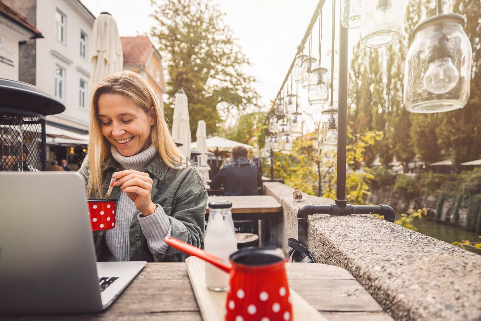 Smiling blonde woman having coffee in the city center, while working on her laptop by VisualProductions