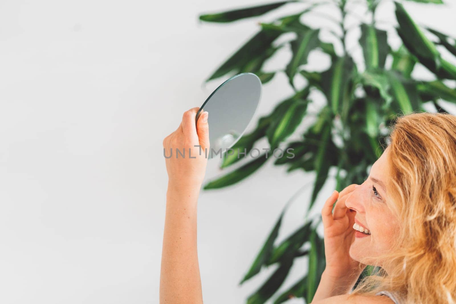 Side view of a woman holding a small mirror high up looking at it while doing her makeup by VisualProductions